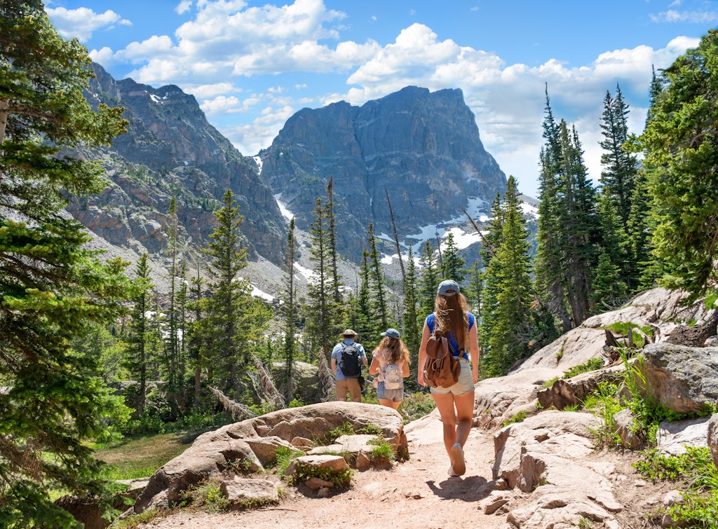 Two girls and their father hike on Emerald Lake Trail through Rocky Mountain National Park with jagged peaks in the distance